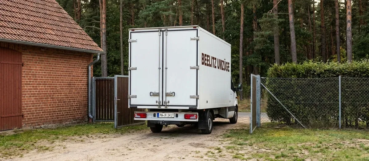Umzugswagen rangiert rückwärts durch eine Hofeinfahrt auf ein sandiges Grundstück